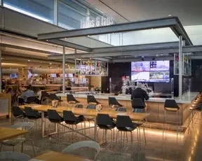 A modern airport bar with tables, chairs, and a lone bartender.