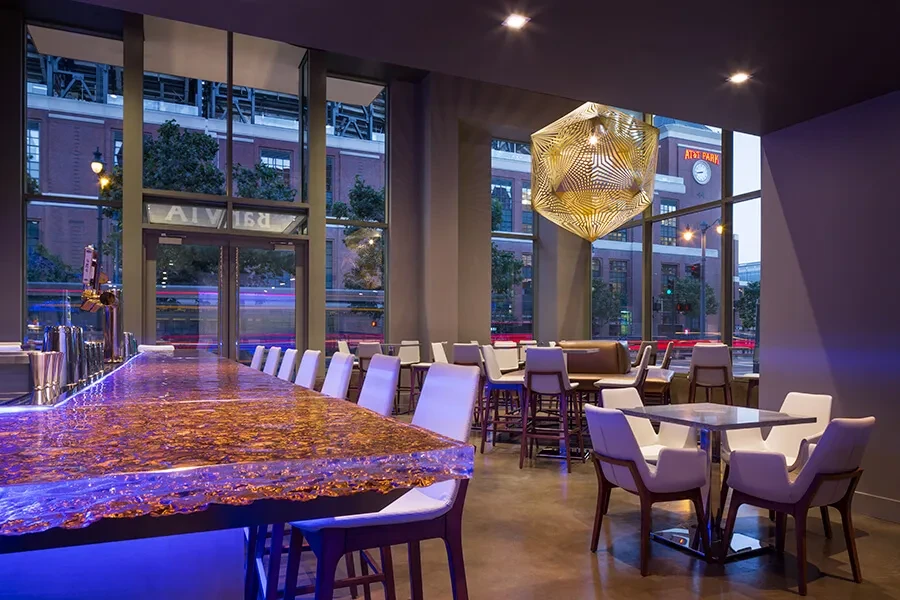 Modern bar with glowing blue counter, geometric chandelier, and city view.