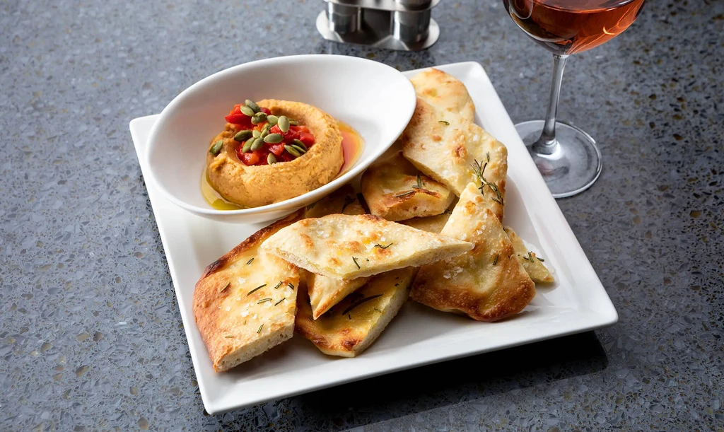 Hummus with red peppers and pumpkin seeds, flatbread, and a glass of wine.