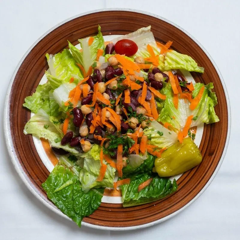 A brown-striped plate holds a salad with lettuce, carrots, beans, and pepper.