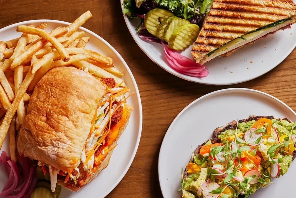 An overhead shot of three plates: sandwich, panini, and avocado toast.