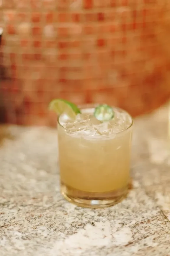 A light drink with lime and green chili on a granite counter.