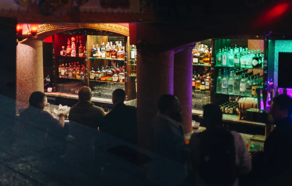 Patrons gathered at a dimly lit bar with numerous liquor bottles displayed.