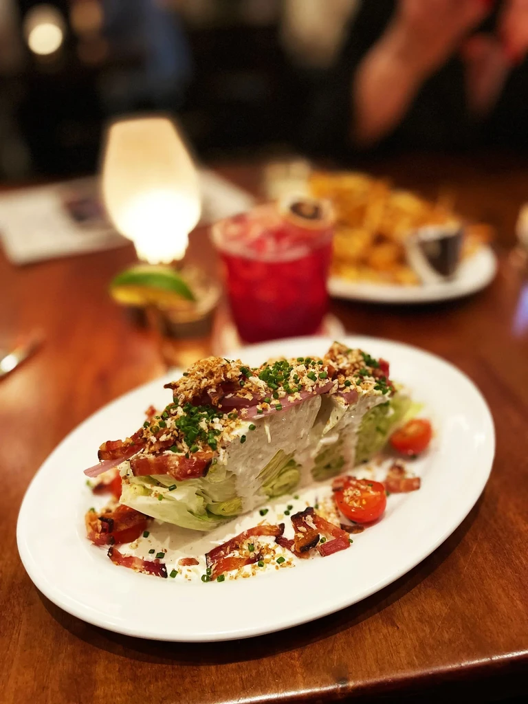 A wedge salad topped with bacon and cherry tomatoes on a white plate.