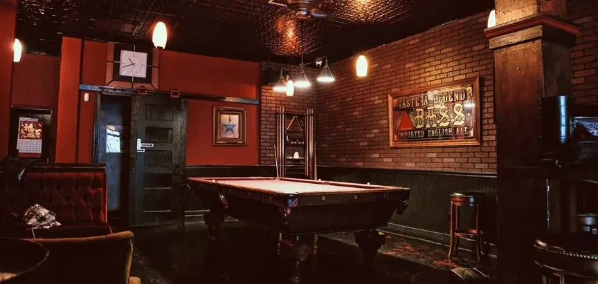 A dimly lit room with a pool table and brick walls.
