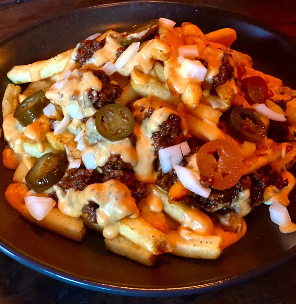 Chili cheese fries topped with onions and jalapenos on a dark plate.