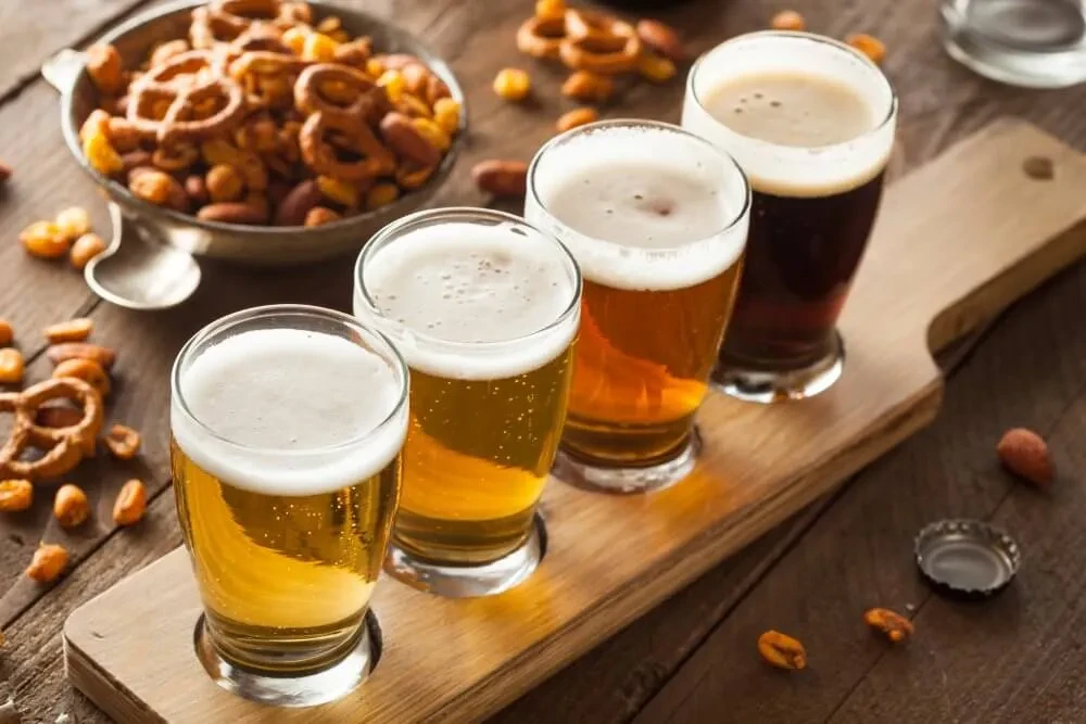A wooden tray holding four beers of varying colors with snacks.