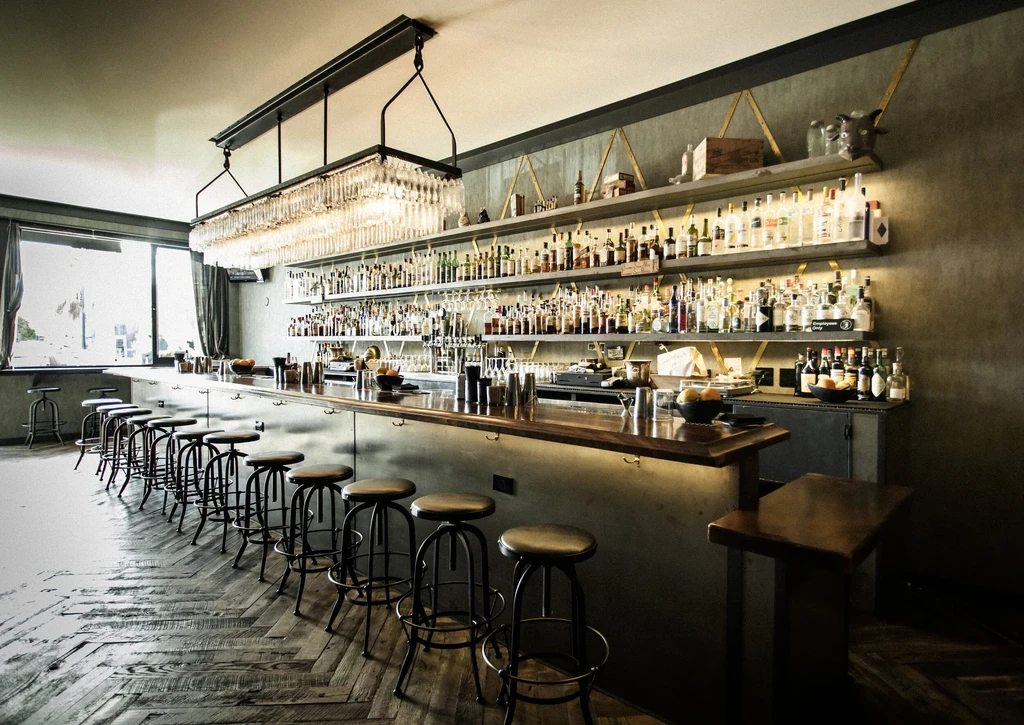 A stylish bar with many liquor bottles and stools along the counter.
