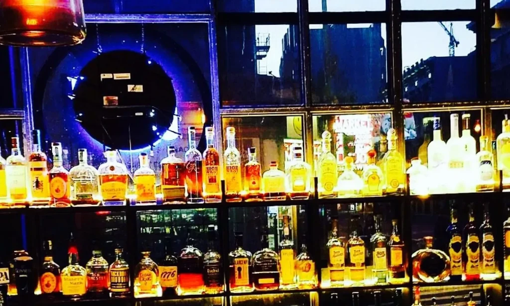 A dimly lit bar with rows of glowing liquor bottles on shelves.