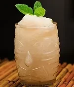 A frosted tiki mug holds a light-colored frozen drink with mint garnish.