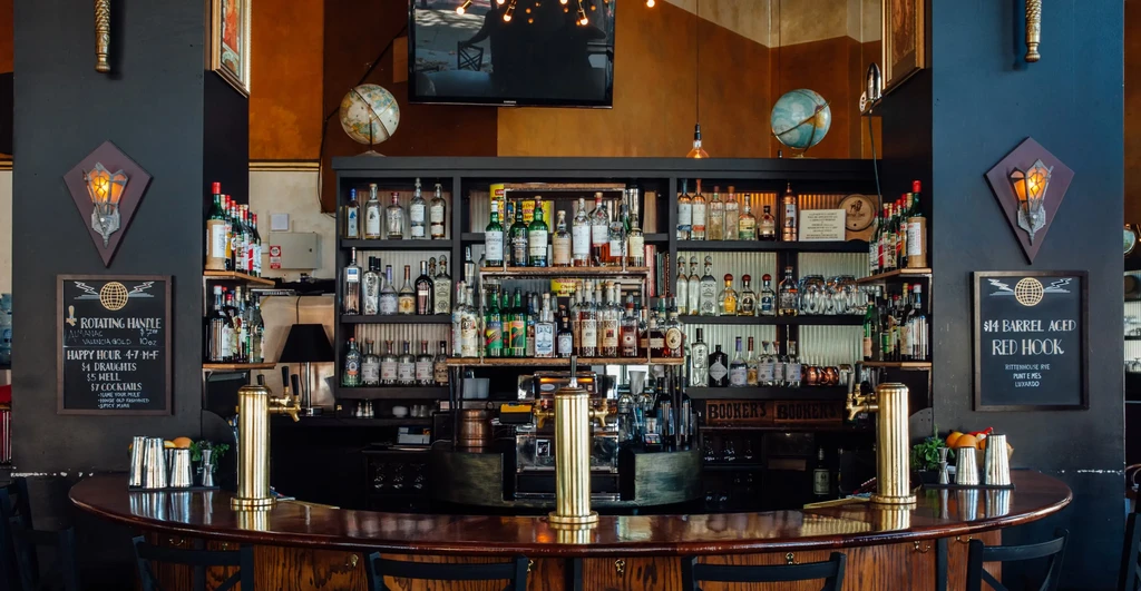 A dark, retro-style bar with a wooden counter and shelves of liquor.