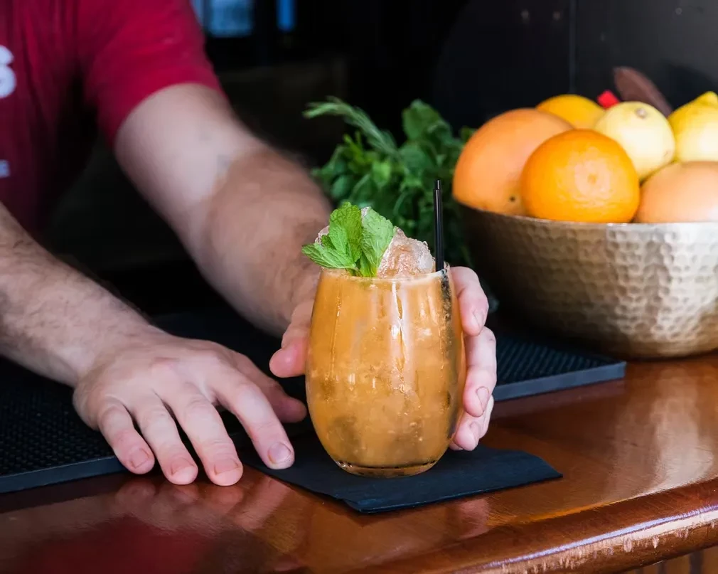 A bartender serves a drink garnished with mint and ice.