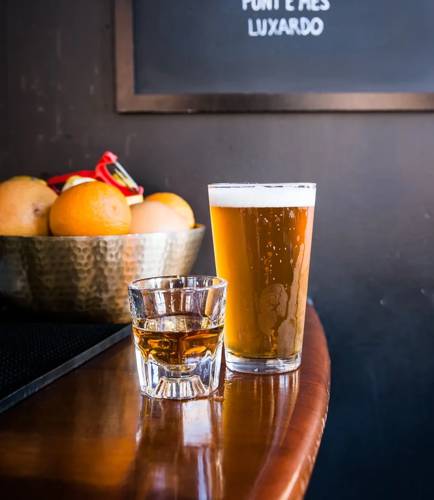 A shot of whiskey and a pint of beer on a wooden table.