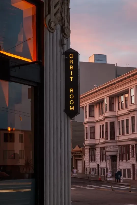 A street scene at dusk with an "ORBIT ROOM" sign.