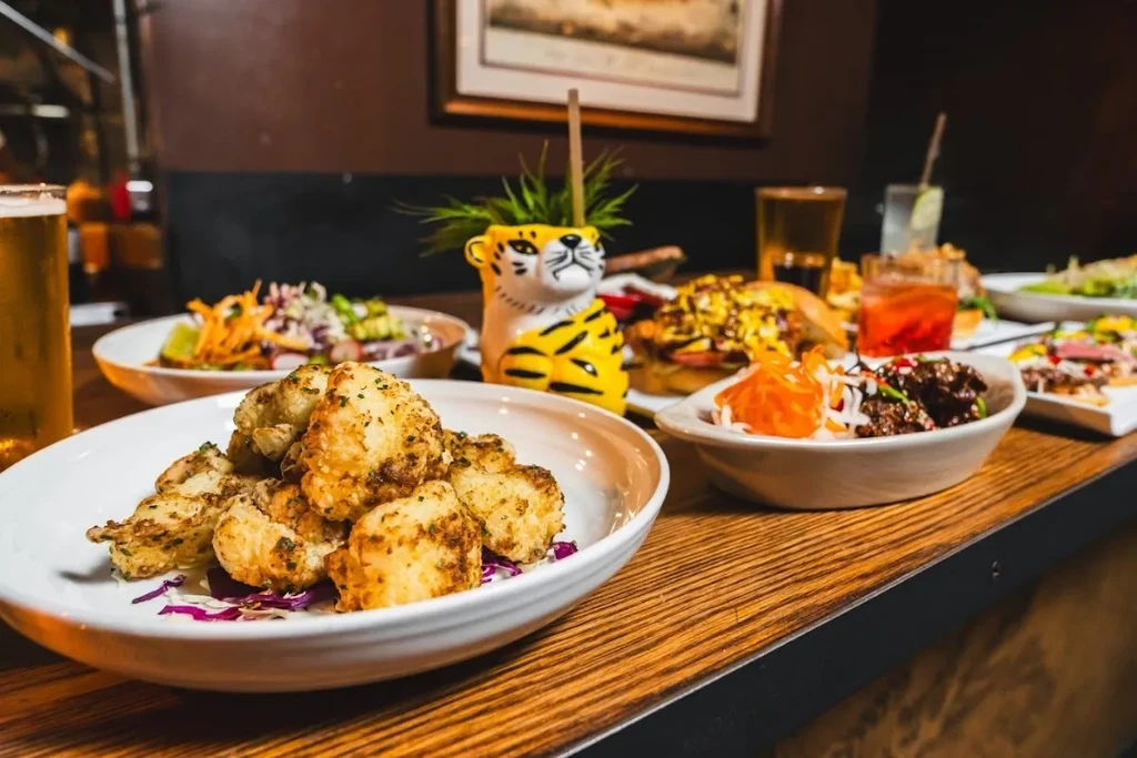 A table laden with various dishes, drinks, and a tiger-shaped planter.