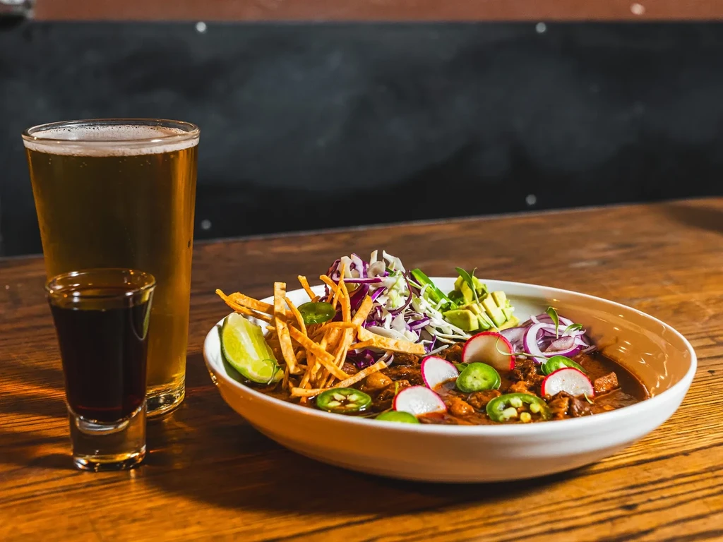A hearty meal with chili, beer, and a shot on a wooden table.