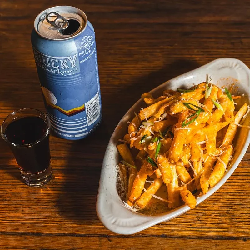 A can of beer, a shot, and fries on a wooden table.