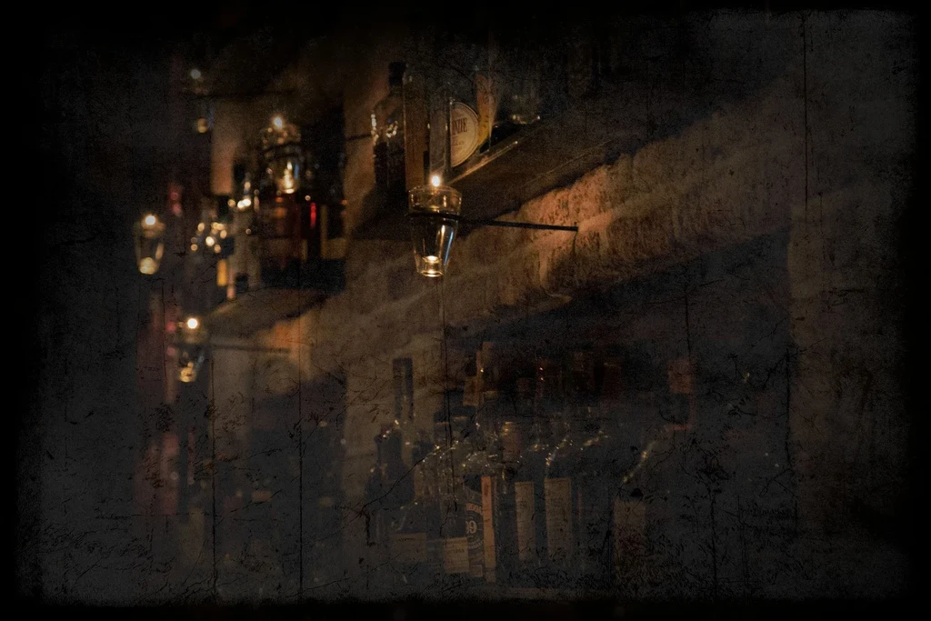 Hanging candles illuminate bottles of liquor in a dimly lit bar.