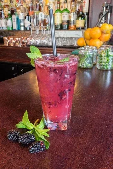 A tall glass of blackberry cocktail with mint garnish and berries.