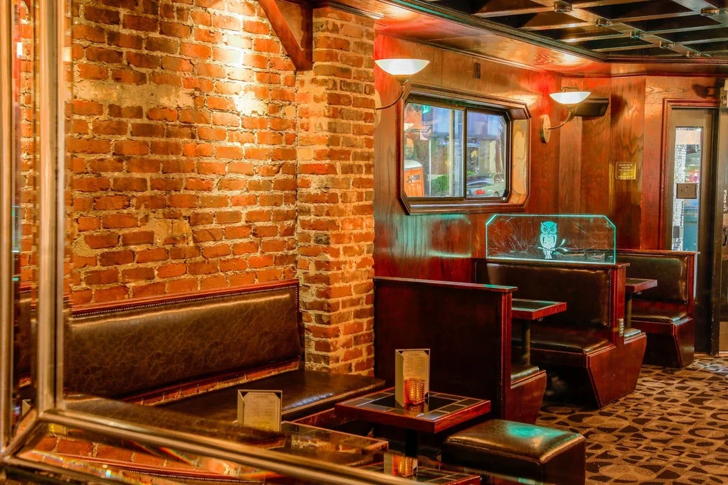 Dark brick wall and wood-paneled bar with booths and a lighted owl.