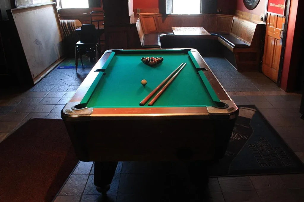 A pool table with racked balls and cues in a dimly lit room.