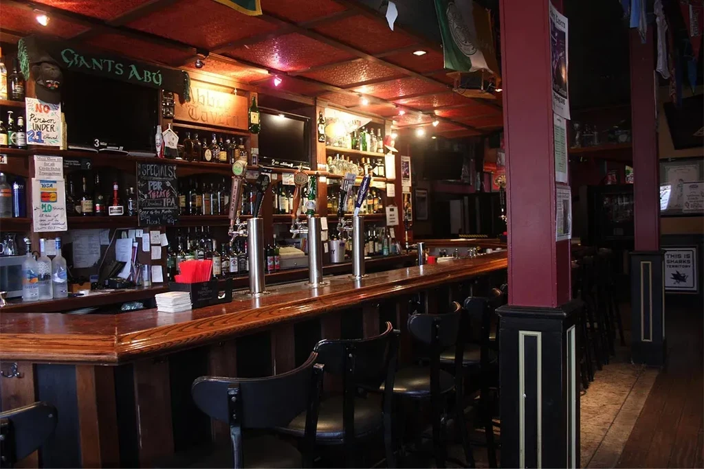 An empty, lit bar with a wooden counter and black bar stools.