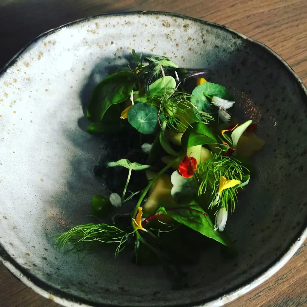 A gourmet salad in a speckled ceramic bowl on a wooden table.