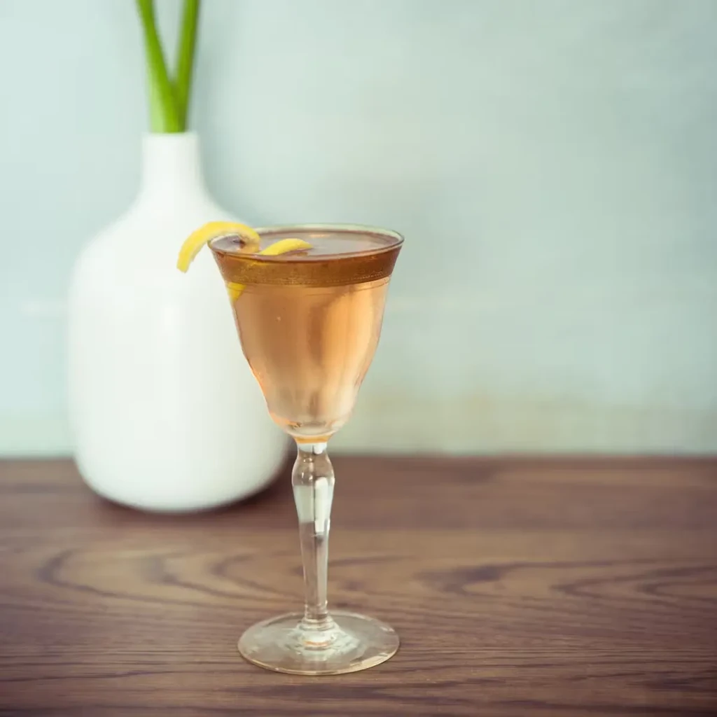 A gold-rimmed cocktail glass with a lemon twist on a wooden surface.