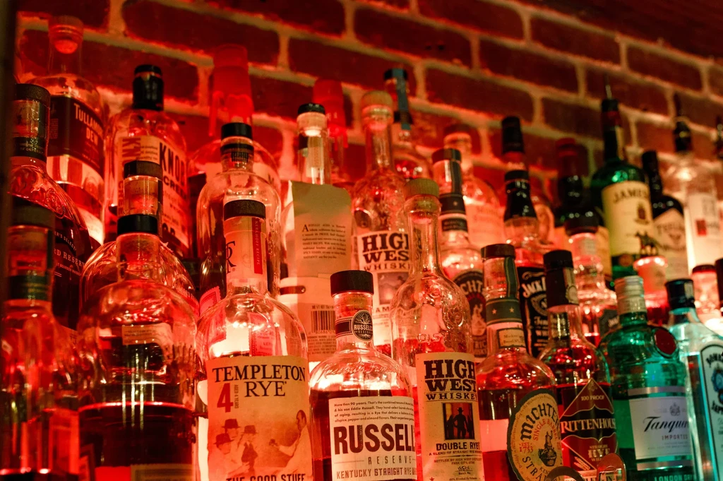 Bottles of whiskey and liquor illuminated by red light against a brick wall.