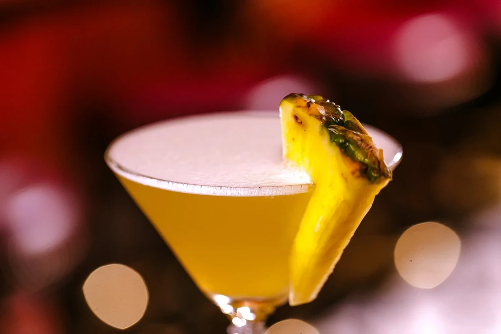 A yellow cocktail with a pineapple slice on the rim.