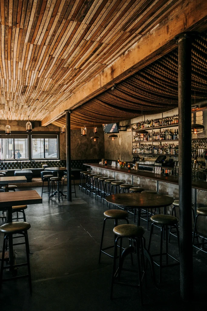 Empty bar with wooden ceiling, industrial accents, and many stools.