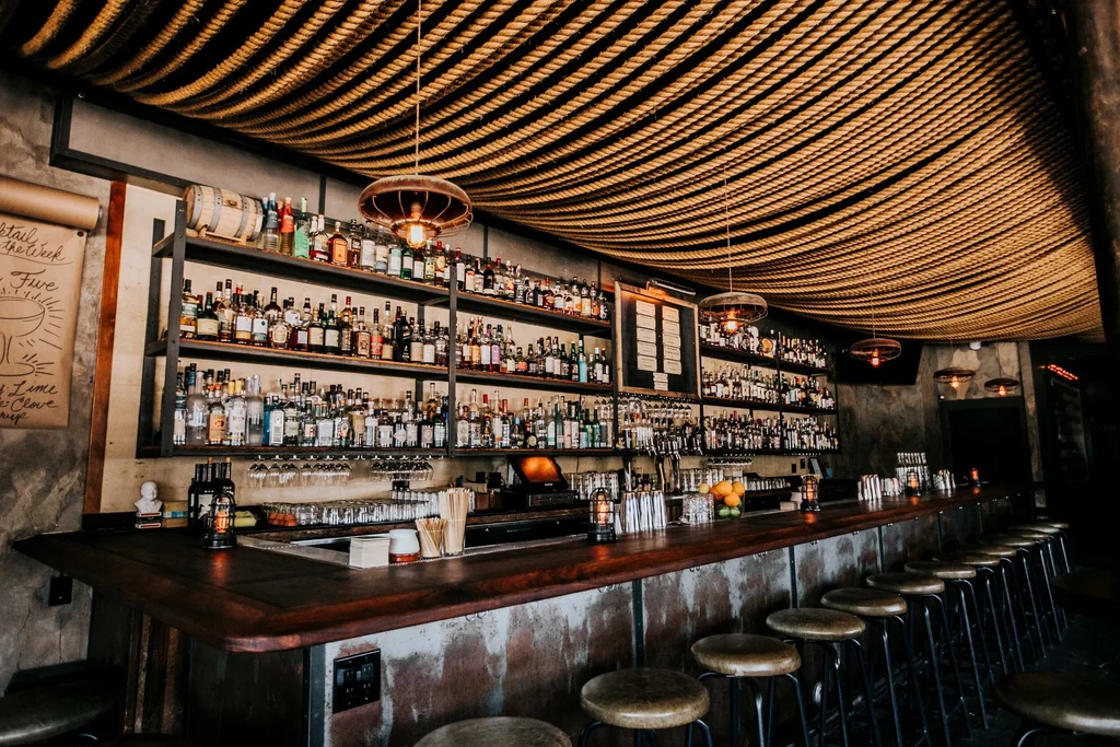 A dimly lit bar with rows of liquor bottles and a rope ceiling.