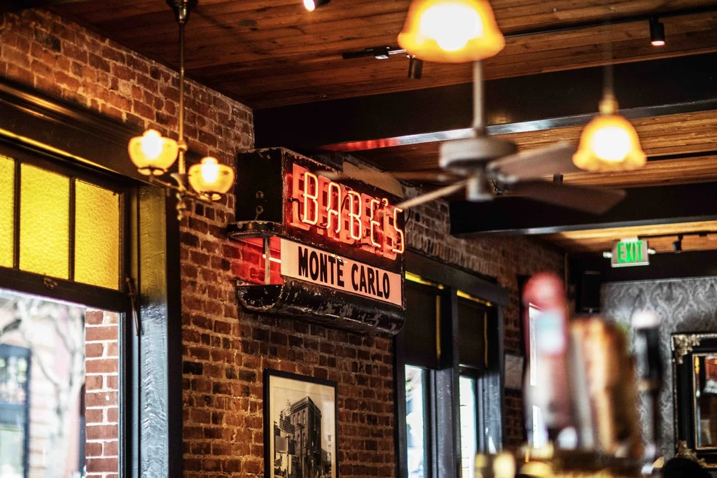 Neon sign for "BABE'S MONTE CARLO" in a brick interior.