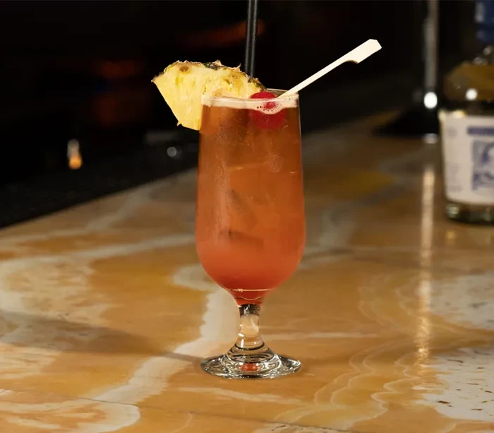 A tropical cocktail with pineapple and cherries on a marble bar.