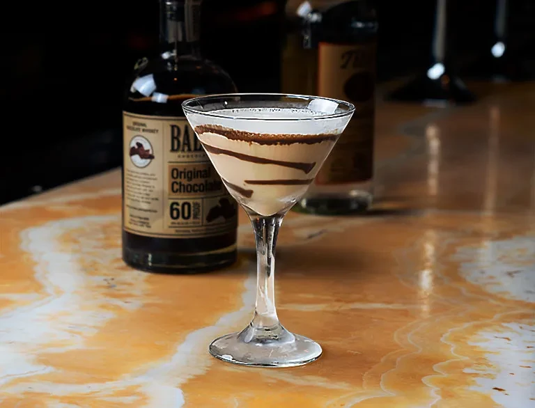 A chocolate martini in a glass next to a chocolate whiskey bottle.