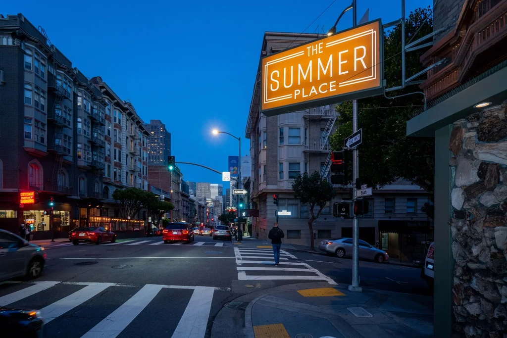 An orange sign for "The Summer Place" above a city street at dusk.