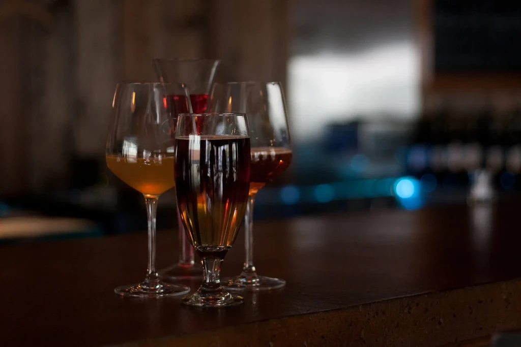 Wine glasses and cocktails on a dark, reflective bar counter.