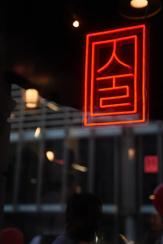 A red neon sign with Korean characters hangs in a dark window.