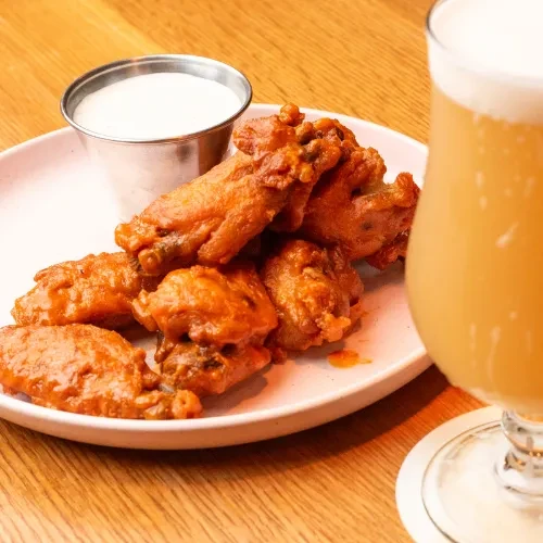 A plate of buffalo wings with dipping sauce and a glass of beer.