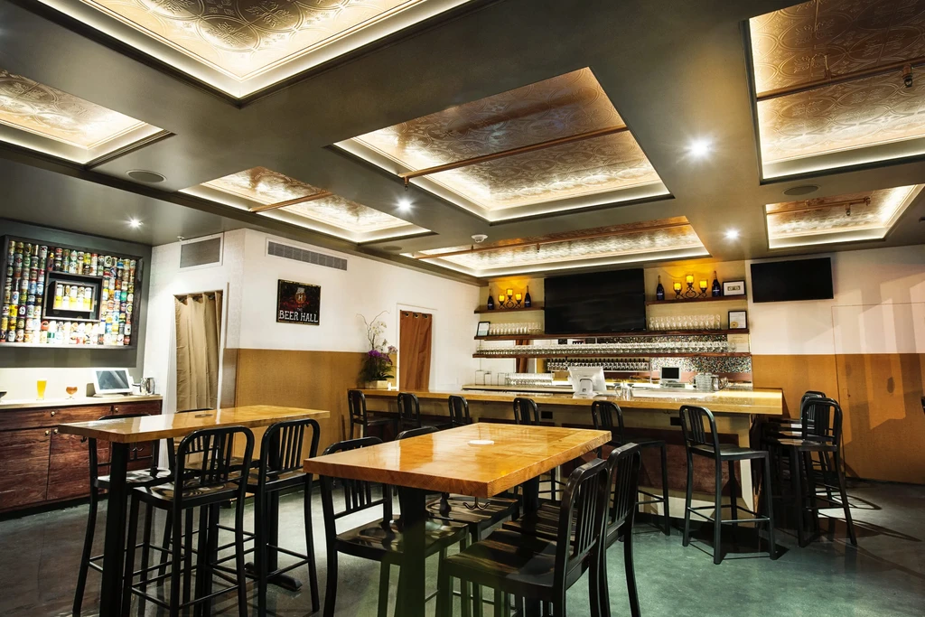 A modern beer hall with high tables and a long bar.