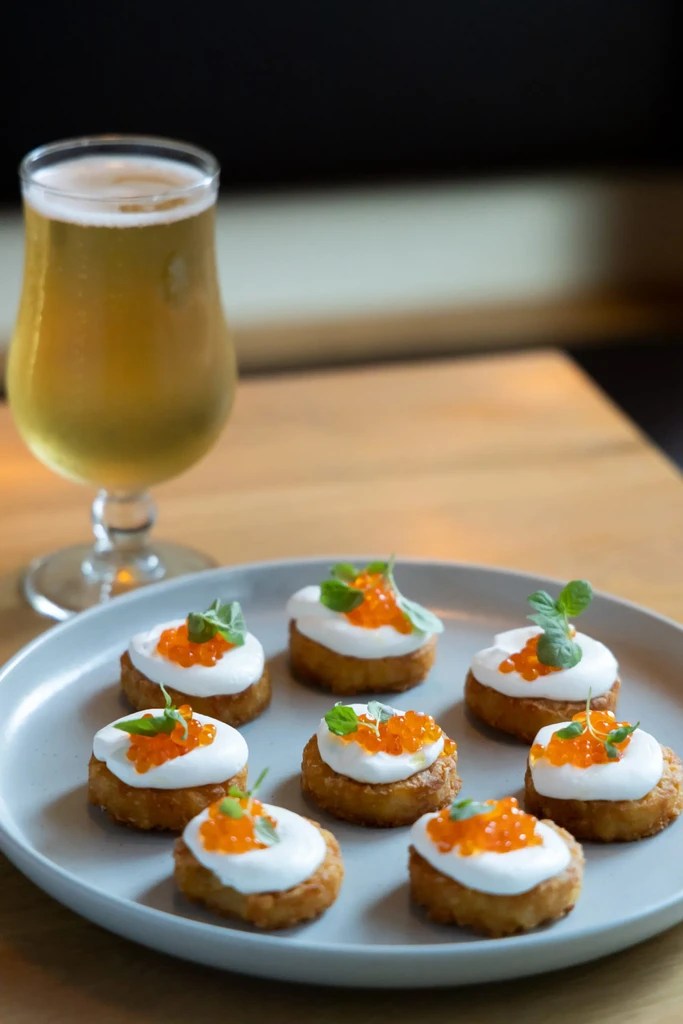 A glass of beer and eight blinis with sour cream and red caviar.