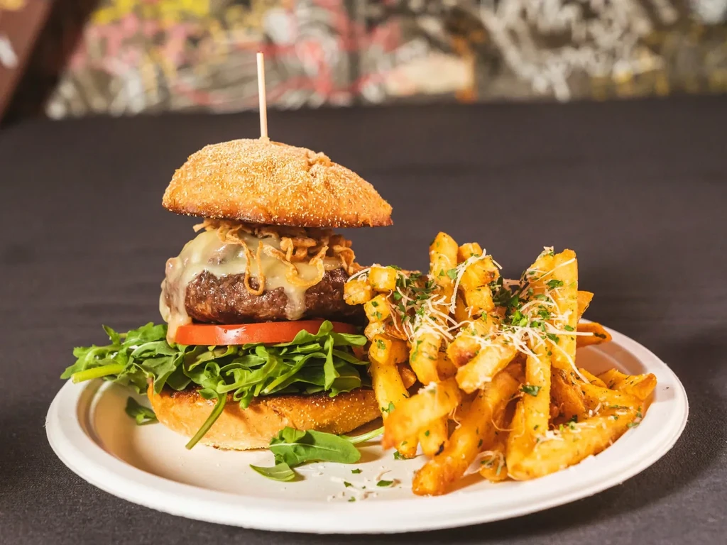 A cheeseburger with fries on a white plate against a dark background.
