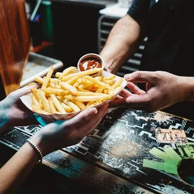 A person's hands receiving a tray of french fries and ketchup.