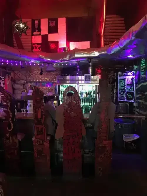 A dimly lit bar with neon lights and decorative wooden carvings.