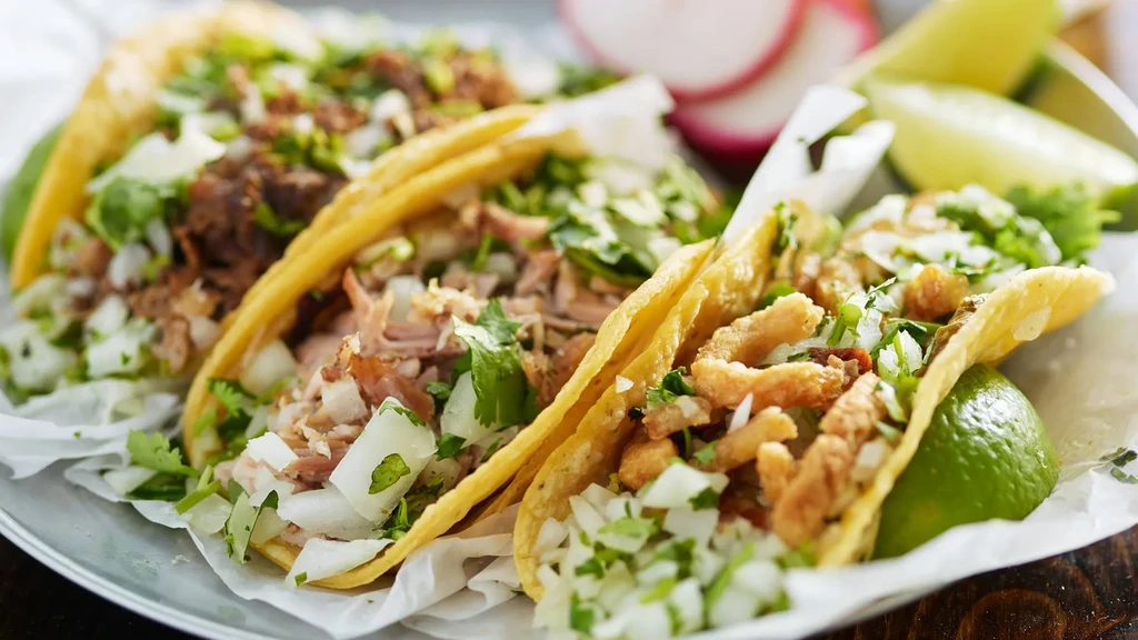 Close-up of a plate of four street tacos with limes and radishes.