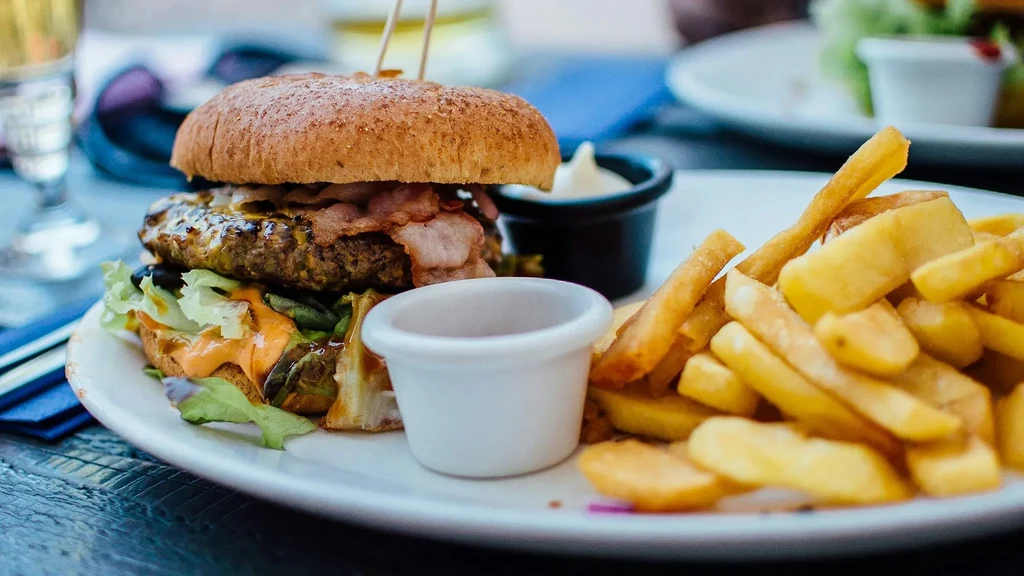 A plate with a bacon cheeseburger, French fries, and two dipping sauces.