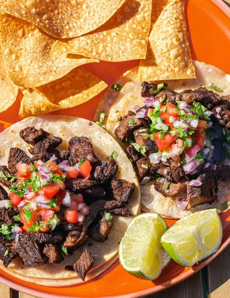 Two beef tacos with pico de gallo, lime, and tortilla chips.