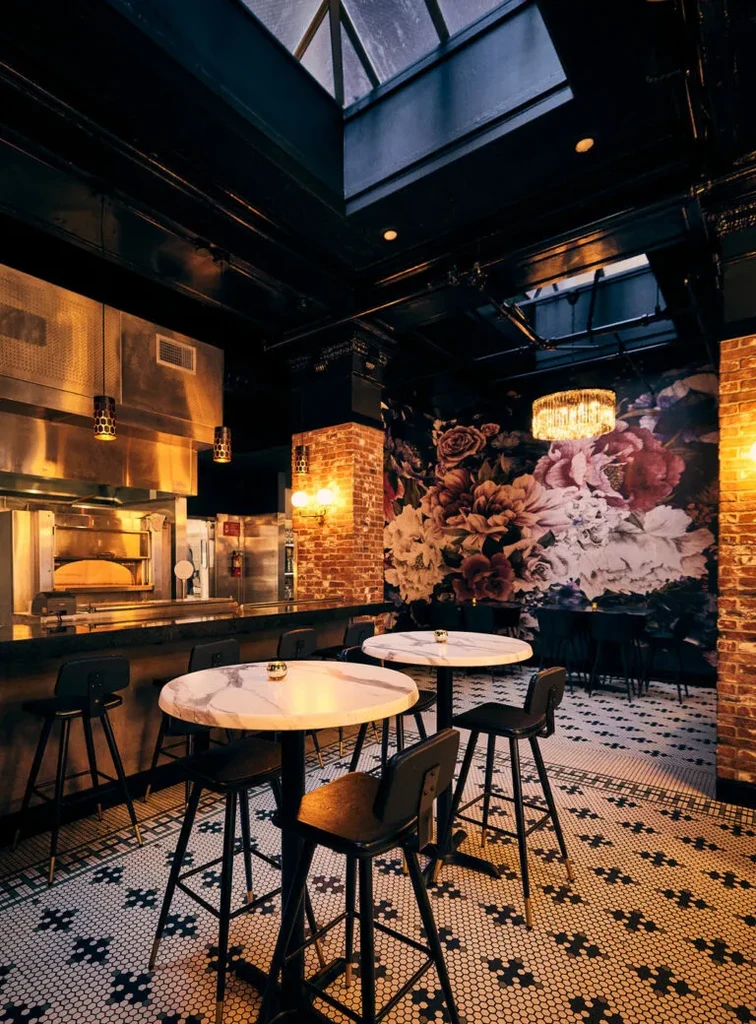 A restaurant with high-top tables, a bar, and a floral accent wall.