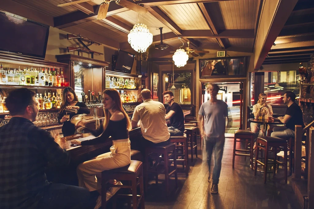 People socialize and drink at a dim, wooden bar.