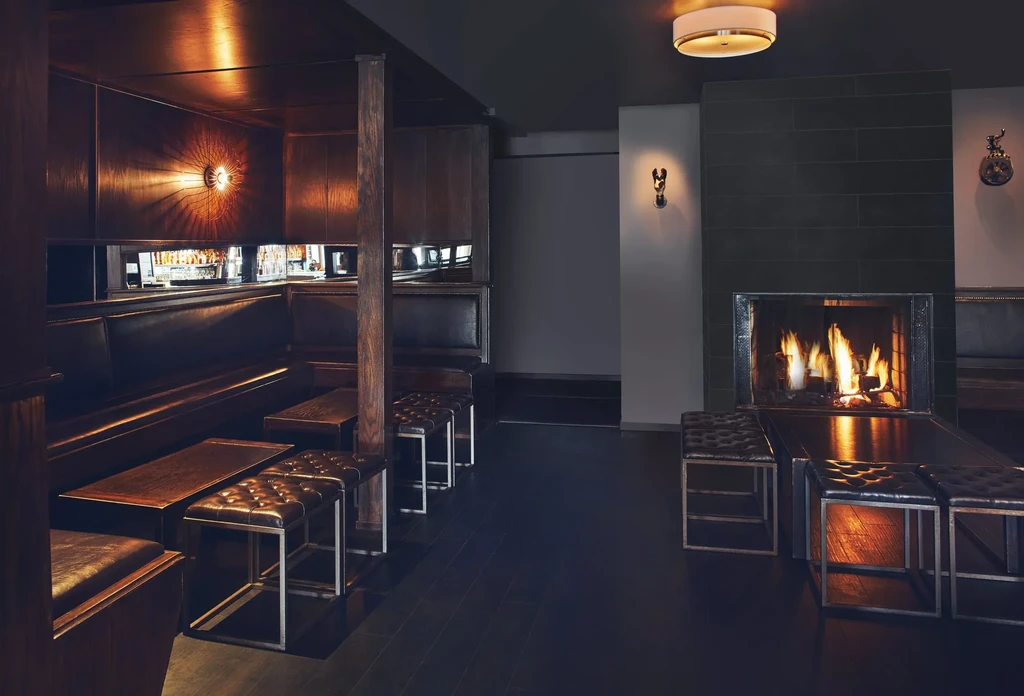 Dimly lit bar interior with booths, tables, stools, and a fireplace.